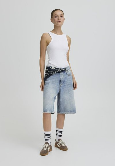 Débardeur blanc à côtes, bermuda en denim bleu clair, bandana noir et blanc noué à la taille, chaussettes rayées blanches et noires, chaussures marron.