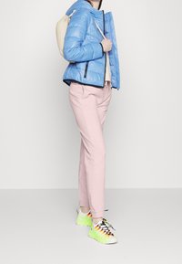 Padded niebieska kurtka z czarnymi akcentami, jasnoróżowe dopasowane spodnie i białe trampki z neonowożółtymi detalami oraz wielokolorowymi sznurówkami.