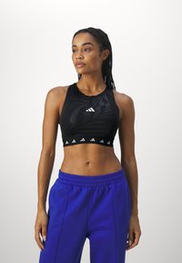 Svart sportsbh med zebra mønster, glidelåsdetaljer og hvit logo; kombinert med høytlivede kongelig blå joggebukser.