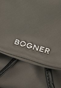 Borsa di stoffa grigia con patta pieghevole e accenti neri, con il logo argento "BOGNER" ben visibile sul davanti.