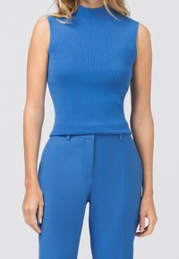 Blå ärmlös topp med hög hals, gjord av ribbad tyg. Matchas med blå skräddarsydda byxor med smal passform.