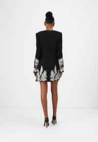 Black dress with long sleeves, featuring white embroidered leaf patterns at the hem and cuffs. Form-fitting silhouette and rear zip closure.