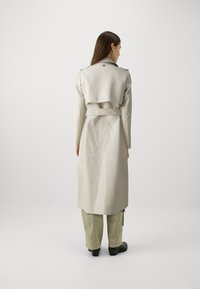 Lichtbeige trenchcoat met een tailleband, lange mouwen en dubbele schouderepauletten. Soepele stof, middelmatig lange ontwerp en minimalistische accenten.