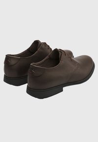 Brown leather shoes with a rounded toe, lace-up design, and contrasting black rubber sole. Minimalist design with subtle stitching details.