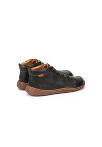 Zapatos de caña alta de cuero verde oscuro con un acabado texturizado, suelas de goma marrón, seis ojales y un forro interior marrón claro.