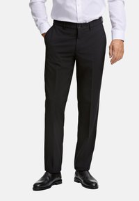 Zwarte pantalon met een getailleerde pasvorm, een vlakke voorkant en zijzakken. Gemaakt van gladde stof, gecombineerd met zwarte leren schoenen.