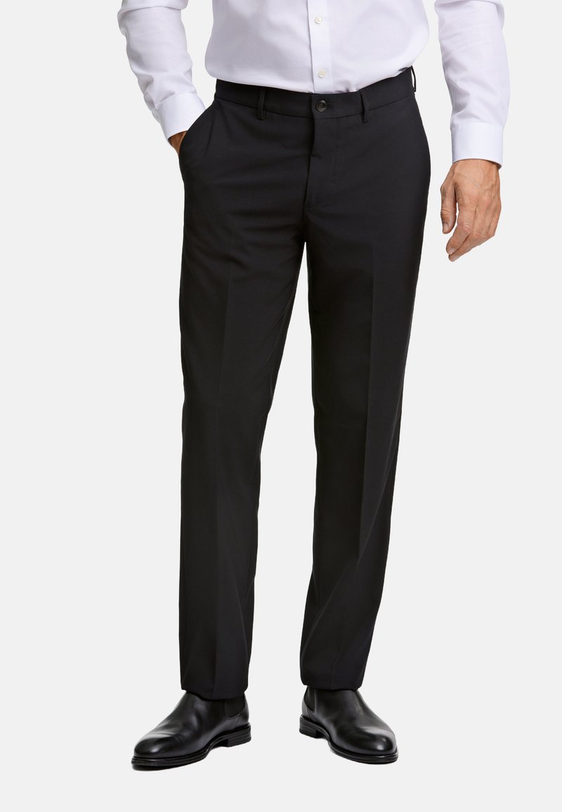 Zwarte pantalon met een getailleerde pasvorm, een vlakke voorkant en zijzakken. Gemaakt van gladde stof, gecombineerd met zwarte leren schoenen.