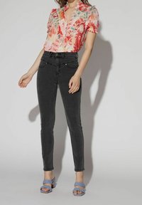Blouse fleurie avec des détails froncés en rose et rouge, associée à un jean skinny noir et des sandales tressées bleu clair.