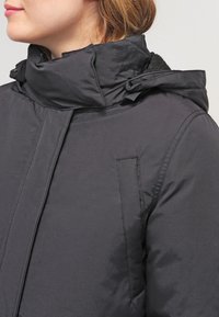 Black padded jacket featuring a high collar, zippered front, and side pockets. Material appears smooth with a soft inner texture.