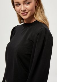 Crni pamučni dukserica s okruglim izrezom, napuhanim dugim rukavima i prilagođenom siluetom. Glatka tekstura, bez uzoraka ili akcenata.