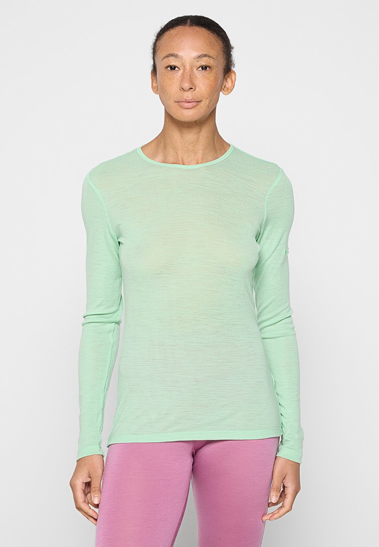 Mintgrünes Langarmshirt mit Rundhalsausschnitt und leichtem, strukturiertem Stoff. Kombiniert mit rosa Leggings. Einfaches, figurbetontes Design.