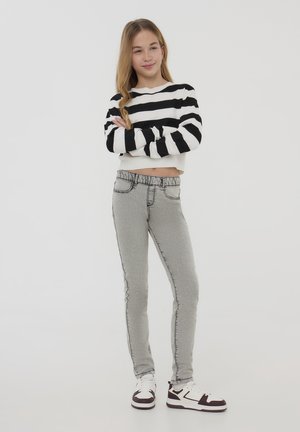 Jeans grigi, elasticizzati, con dettagli di cucitura laterali e vita elastica, abbinati a un top corto a righe bianche e nere e sneakers.