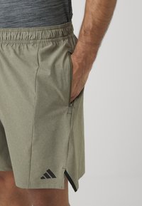 Kaki shorts med en tekstureret finish, elastisk talje, sidelommer og et sort Adidas-logo nær sømmen. Har sidespalter for nem bevægelse.