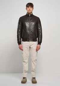 Donkerbruine leren bomberjack met geribde manchet- en kraag, gecombineerd met lichtbeige cargobroek en taupe veterschoenen.