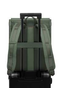 Olijfgroene rugzak met gewatteerde schouderbanden en een uitschuifbare zwarte handgreep, bevestigd aan een zwarte kofferbasis met wielen. Gestructureerd oppervlak en ritsen.