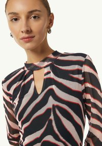 Haut transparent à manches longues avec un motif zèbre en noir, beige et rouge. Présente un décolleté en forme de clé et un col arrondi.