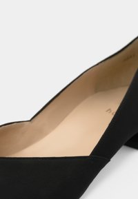 Black suede flat shoe with a pointed toe and a smooth, cream-colored interior lining. The design features stitching along the edge.