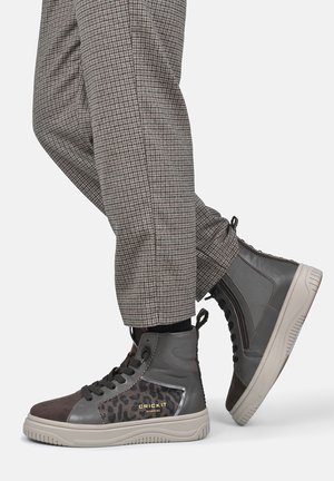 Graue High-Top-Sneaker mit Leopardenmuster-Akzenten, getragen zu braunen karierten Hosen vor einfarbigem Hintergrund.