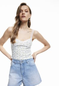 Blommig tryckt linne med spetsdetaljer, vit bakgrund, figursydd design. Kombinerat med ljusblå högmidjade denimshorts med fransad nederkant.