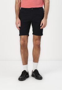 Black shorts made from a lightweight material, featuring a button closure, side pockets, and rolled hems. Pairing with black shoes and white socks.