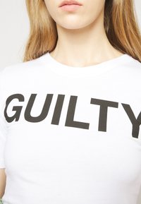 Camiseta blanca de algodón con letras negras en negrita que dicen "CULPABLE". La tela tiene una textura suave y un diseño de cuello redondo estándar.