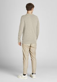 Suéter de punto beige claro con mangas largas, cuello redondo y puños de canalé; combinado con pantalones beige ajustados y zapatillas blancas.