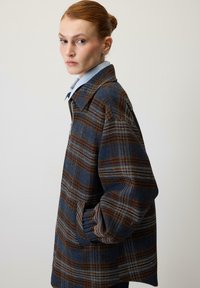 Jakna s karo vzorcem v modrih, rjavih in belih odtenkih, izdelana iz teksturirane tkanine z ovratnikom in stranskimi žepi.