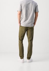 Olijfgroene katoen broek, slim fit, met platte voorkant, met een gladde textuur. Gekocht met een grijs T-shirt met korte mouwen en witte sneakers.