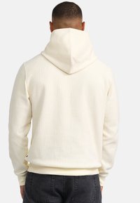 Hoodie color crema con motivo testurizzato, dotato di un ampio cappuccio, polsini e orlo a costine, e un design minimalista.