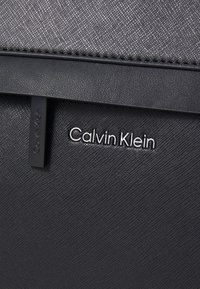 Černá texturovaná peněženka s hladkým povrchem, vybavená stříbrným logem "Calvin Klein" a minimalistickým designem.