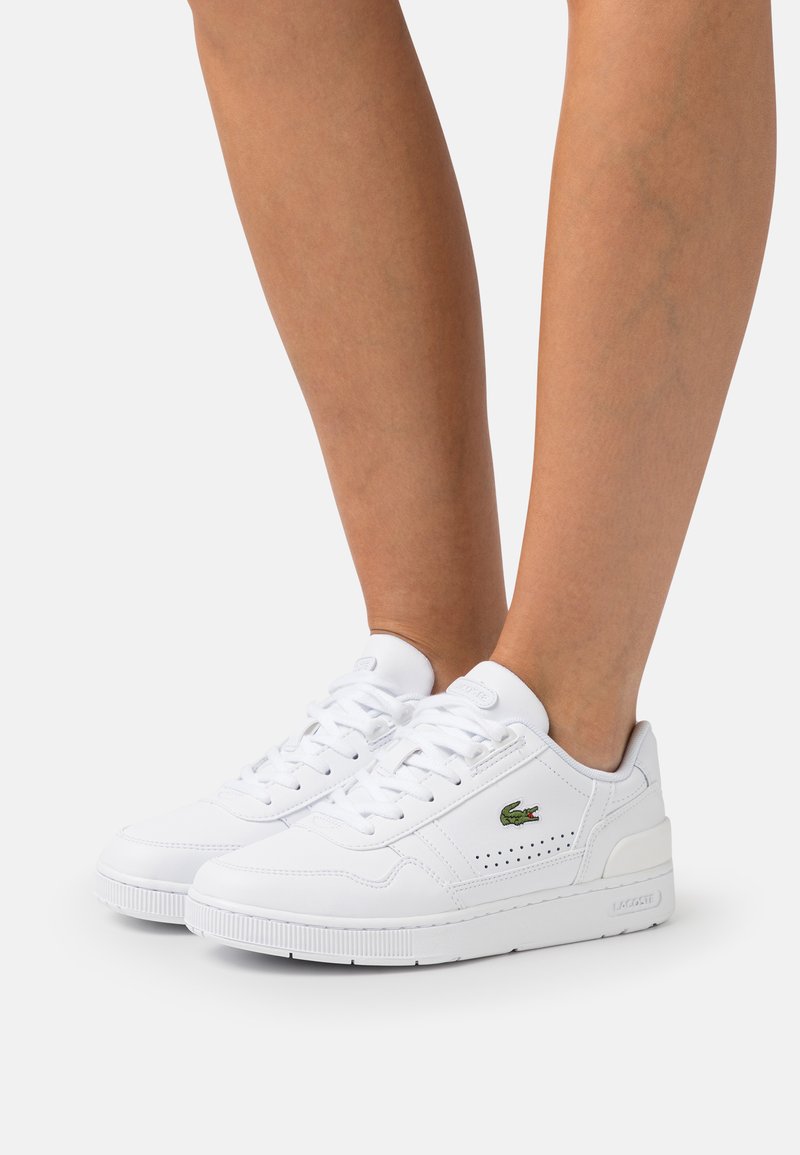 Białe skórzane sneakersy z perforowanymi akcentami i zielonym haftowanym logo. Posiadają zaokrąglony czubek oraz teksturowaną gumową podeszwę.