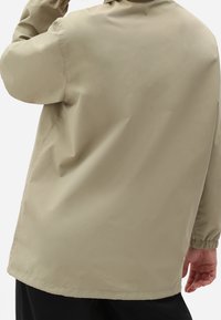 Beige, lätt jacka med avslappnad passform, långa ärmar och elastiska muddar. Slät textur, fållen slutar under midjan.