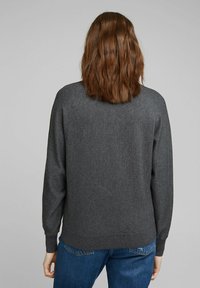 Donkergrijze trui van zacht materiaal met een relaxte pasvorm, ronde halslijn, en geribde manchetten en zoom, gedragen over blauwe jeans. Zicht van achteren.