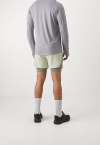 Conjunto deportivo para hombres que incluye una camiseta de manga larga gris, pantalones cortos verde claro y zapatillas negras. Calcetines blancos visibles, los pantalones cortos tienen un detalle de acento.