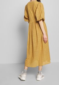 Gul perforerad midiklänning med puffärmar, midja med innyttning och en flödande kjol. Bärs med vita sneakers och grå strumpor.