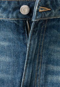 Detailný záber modrých džínsov s kovovým gombíkom označeným "MC Jeans" a čiastočne rozopnutým zipsom, ktorý odhaľuje oranžové prešívanie.