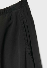 Elastic waistband black pants with side slit pocket and visible stitching on smooth fabric.