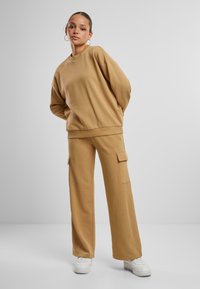 Brauner Baumwoll-Sweatshirt mit lockerem Schnitt, kombiniert mit passenden weiten Cargo-Hosen mit Seitentaschen. Abgerundet mit weißen Sneakers.