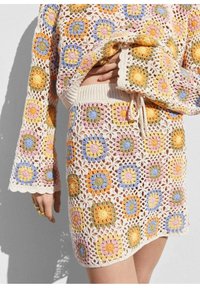 Ensemble deux pièces en crochet avec manches longues et jupe présentant des motifs floraux carrés colorés en orange, jaune, bleu, rose et vert.