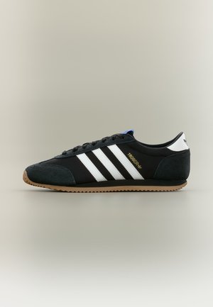 Czarny sneaker Adidas z białymi paskami, gumową podeszwą i złotym napisem „1689ER” po boku, pokazany zewnętrznym profilem.