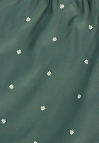 Tissu vert foncé avec de petites marguerites blanches dispersées, dotées de cœurs jaunes, créant un motif floral subtil sur une texture lisse.