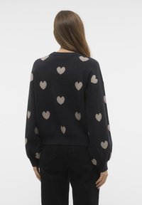Stickad tröja i marinblått med en cropped design. Har beige hjärtmönster och ballongärmar. Mjuk textur, rund halsringning.