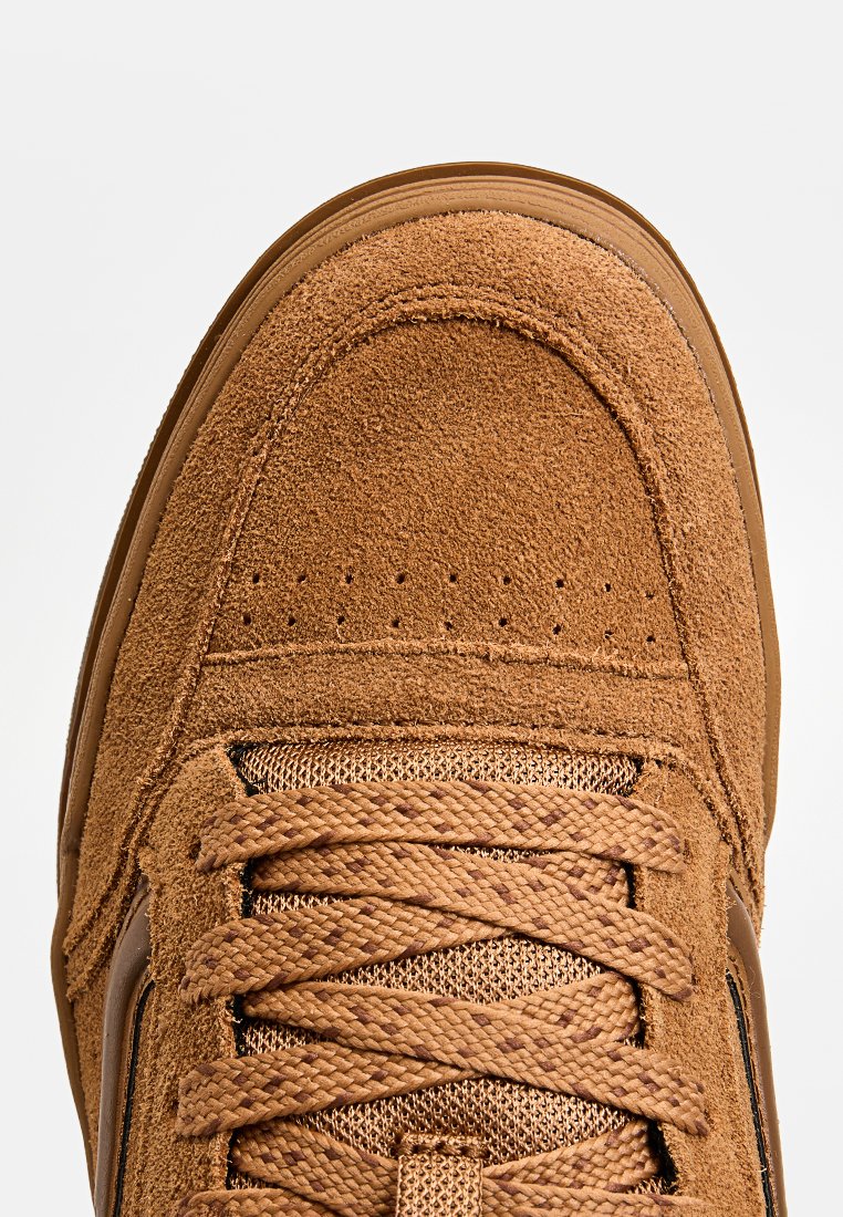 Sneaker in suede marrone con superficie testurizzata, punta perforata e lacci intrecciati. Presenta una suola in gomma e accenti laterali in contrasto.