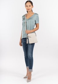 Lys teal satinbluse med V-udskæring, parret med slidte blå jeans og grå høje hæle. Hvid skuldertaske med frynse detalje.