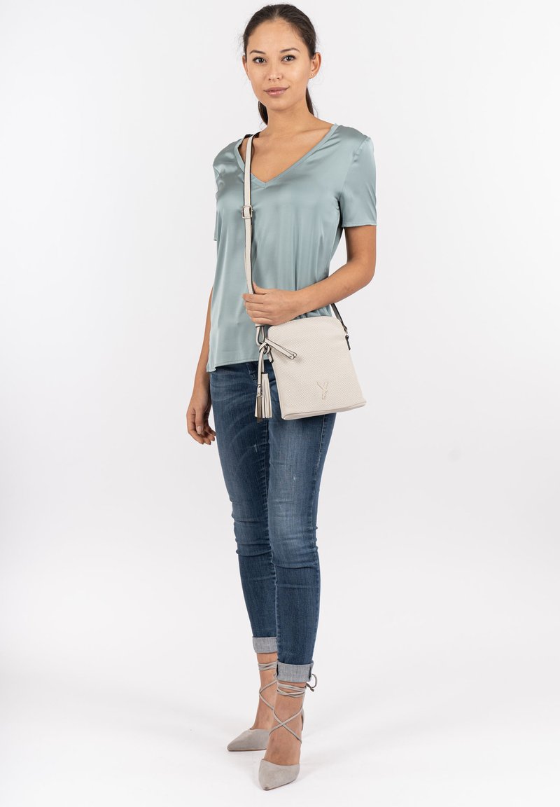 Lys teal satinbluse med V-udskæring, parret med slidte blå jeans og grå høje hæle. Hvid skuldertaske med frynse detalje.