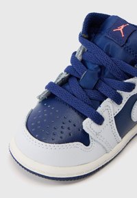 Plave i bijele kožne tenisice s perforiranim vrhom, mornarskim vezicama i malim crvenim Jumpman logom na jeziku na bijeloj pozadini.