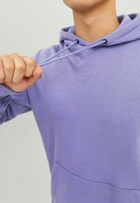 Felpa viola realizzata in tessuto morbido, con tasca frontale, cappuccio con cordino e polsini a coste. Finitura texturizzata con dettagli minimali.