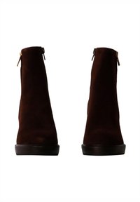 Botas de tobillo de ante marrón con una textura suave, punta redondeada y cremalleras laterales. Diseño minimalista con una suela negra baja.