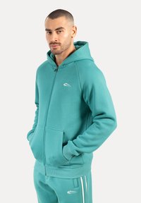 Turkoise zip-up hoodie met een kangoeroezak en geribbelde manchetten. Bevat een klein logo op de borst, gemaakt van zacht, textured materiaal.