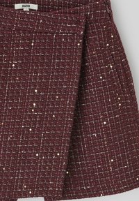Jupe texturée bordeaux en tissu tissé à motif écossais avec des sequins dorés éparpillés. Dispose d'une ceinture lisse et d'un design plissé.